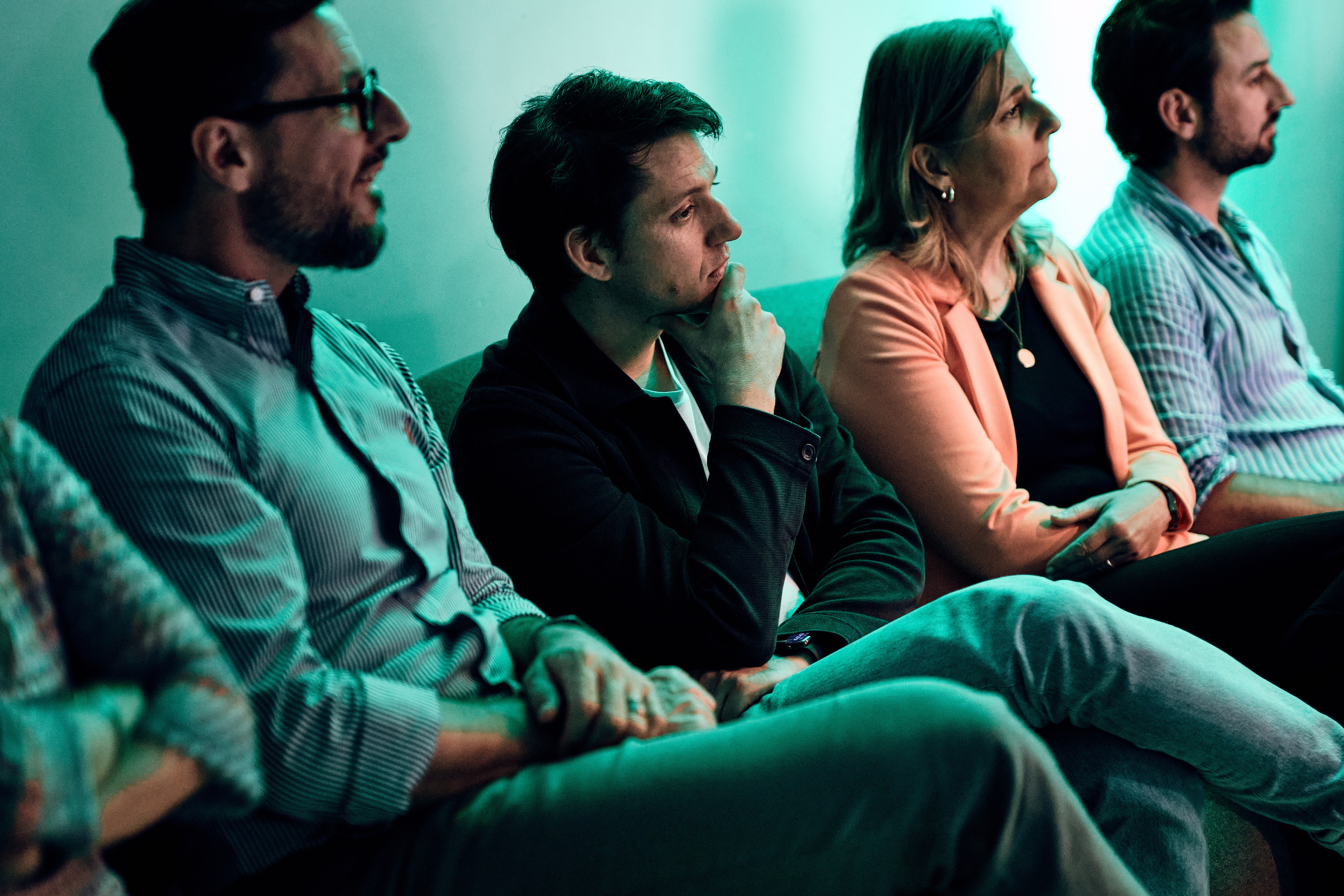 Vier Personen sitzen dicht beieinander in einem schwach beleuchteten Raum und konzentrieren sich auf etwas außerhalb des Rahmens.